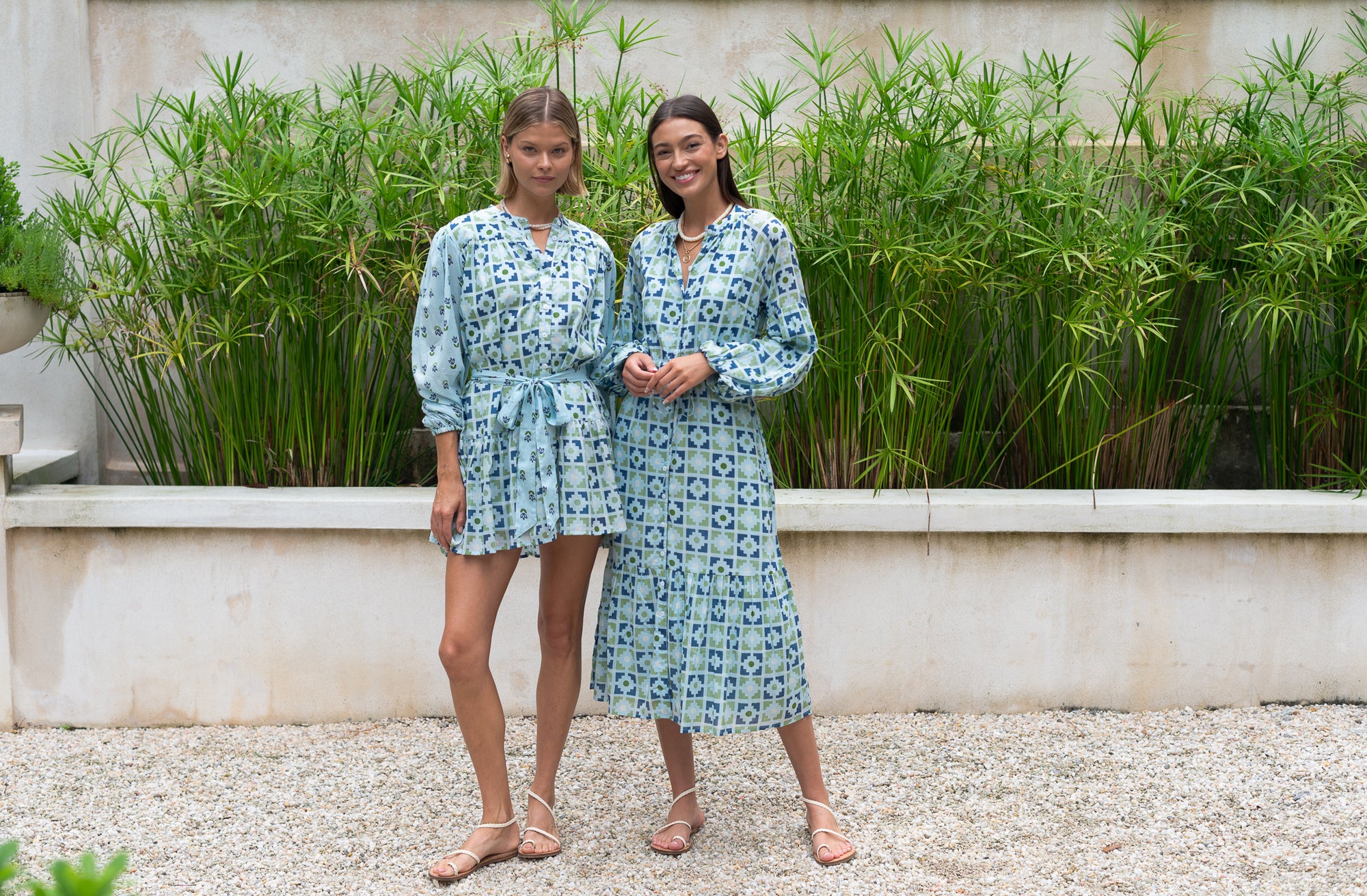 Two women wearing light blue dresses standing in front of a bamboo planter.